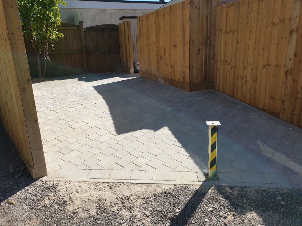 Image of a driveway with country cobble and a border, surrounded by fencing and a retractable safety bollard at the end. The end of the garden is gravelled with dorset gravel.