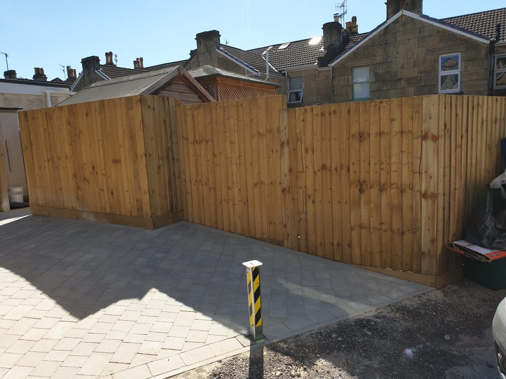 Image of a driveway with country cobble and a border, surrounded by fencing and a retractable safety bollard at the end. The end of the garden is gravelled with dorset gravel.