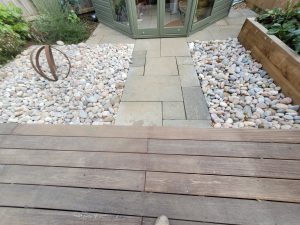 Garden landscaping project in Mells with Hardwood Balau Deck, Kandla Grey Sandstone Paving, Flowerbeds, Scottish Pebbles, and Slatted Fence Panels